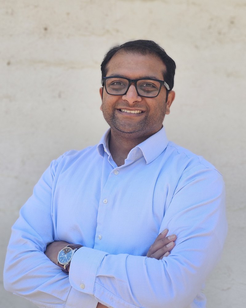 Javin Oza, principal investigator of the Oza Lab, smiling with arms crossed